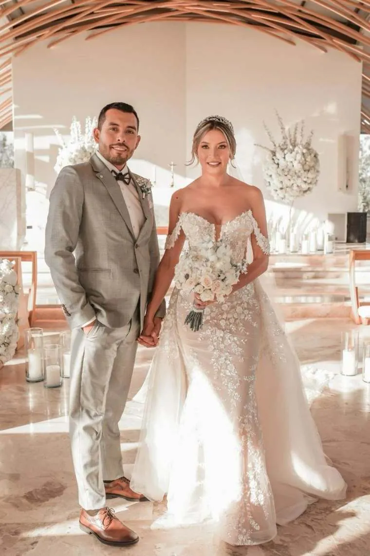 Novios tomados de la mano en el altar blanco de la capilla con un ramo de rosas, boda en Villavicencio