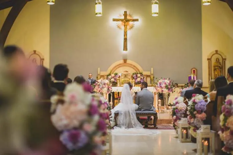Novios sentados ante el altar durante la ceremonia religiosa rodeados de flores, boda en Villavicencio
